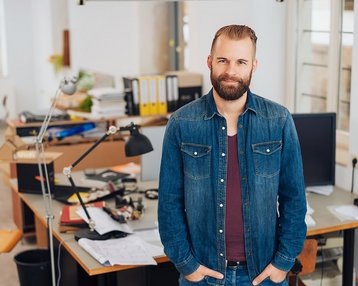 Mann steht im Büro vor Schreibtisch