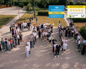 Gruppenszene mit vielen Personen auf einem Platz, die zusammenstehen. Auszeichnungen für eine Fernschule sind im Bild sichtbar.