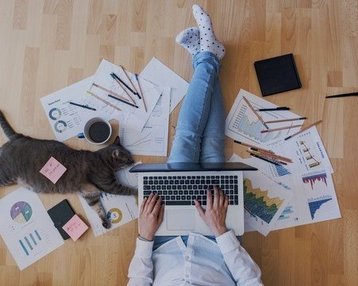 Person auf dem Boden sitzend mit Notebook auf dem Schoß und Papieren um sich herum